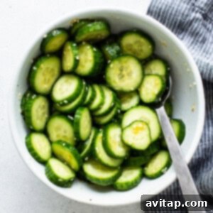 Crisp mini cucumbers tossed in a savory dressing within a white bowl, accompanied by a spoon.