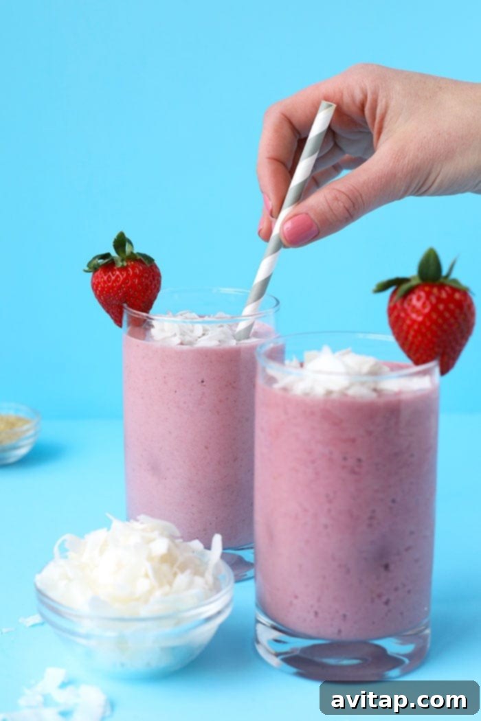 Strawberry Coconut Workout Refuel 4 A refreshing strawberry coconut protein smoothie, garnished with fresh strawberry slices and shredded coconut, invitingly sits ready for consumption after a vigorous workout. It promises a delicious way to replenish nutrients and energy.