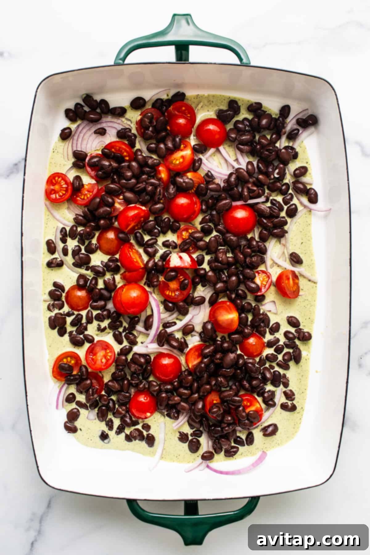Fresh Prep Taco Bowl 4 A baking dish filled with vibrant, fresh ingredients including black beans, halved cherry tomatoes, and thinly sliced red onions, ready for the next layering step of the make-ahead taco salad.