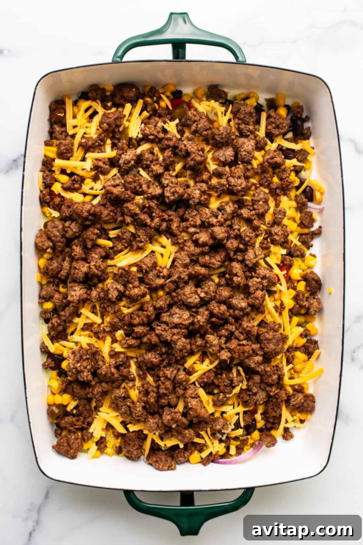 Fresh Prep Taco Bowl 5 A baking dish with neatly arranged layers of seasoned ground beef, vibrant corn kernels, and shredded cheddar cheese, showcasing the strategic layering technique for a make-ahead taco salad.