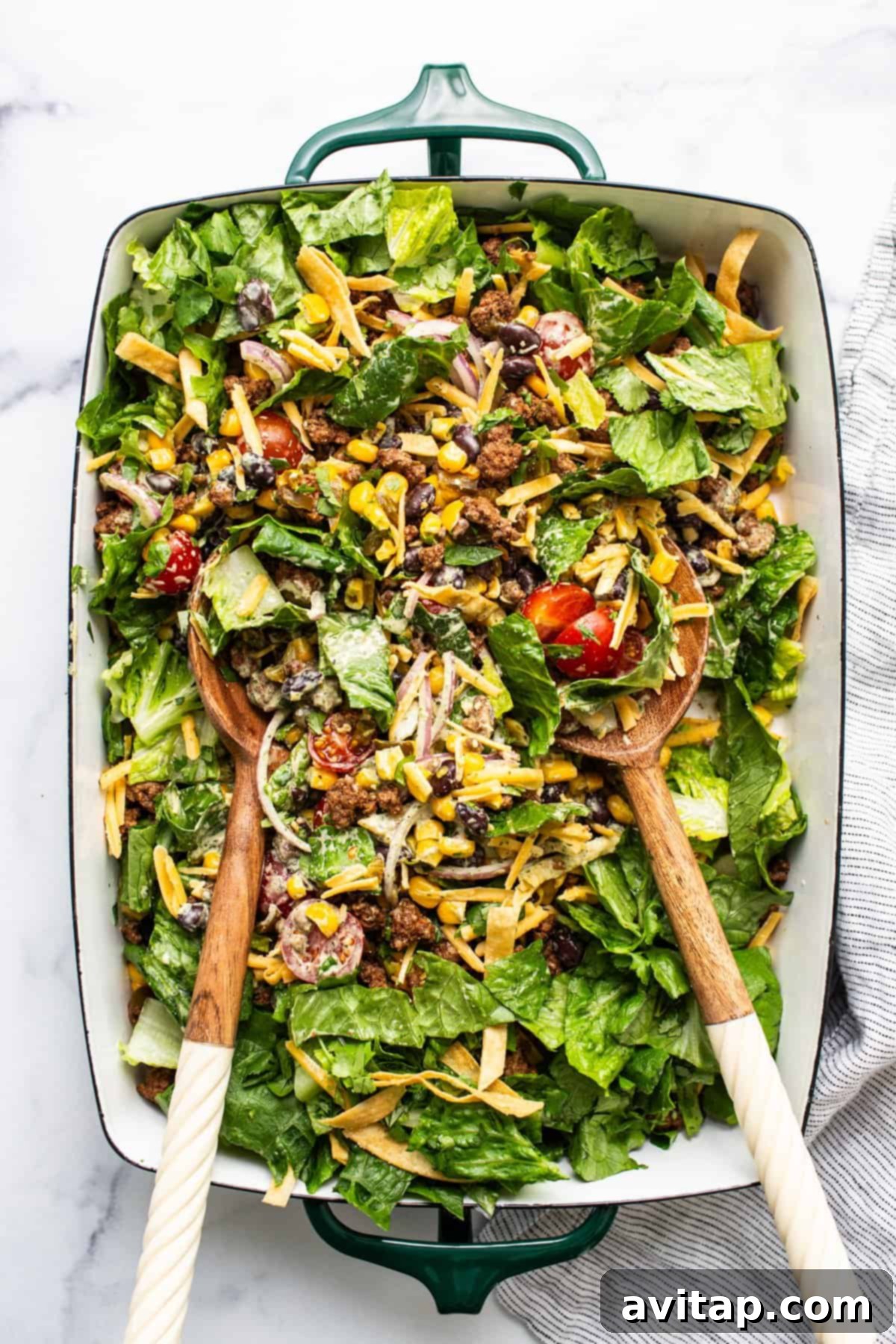 Fresh Prep Taco Bowl 6 A large, vibrant taco salad, beautifully tossed and presented on a green serving platter with wooden serving utensils, showcasing its fresh and abundant ingredients.