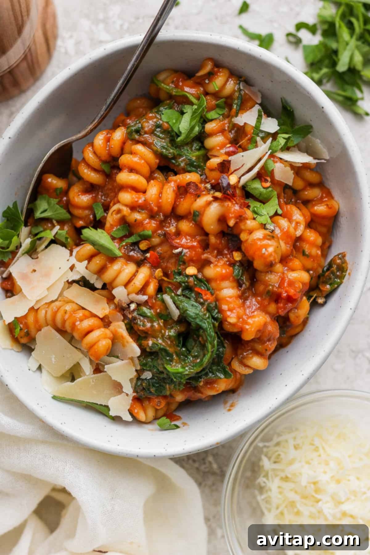 Easy One-Pot Pasta Alla Vodka 2 A vibrant bowl of tomato-based pasta, artfully garnished with fresh spinach and delicate shaved parmesan cheese, ready to be enjoyed.
