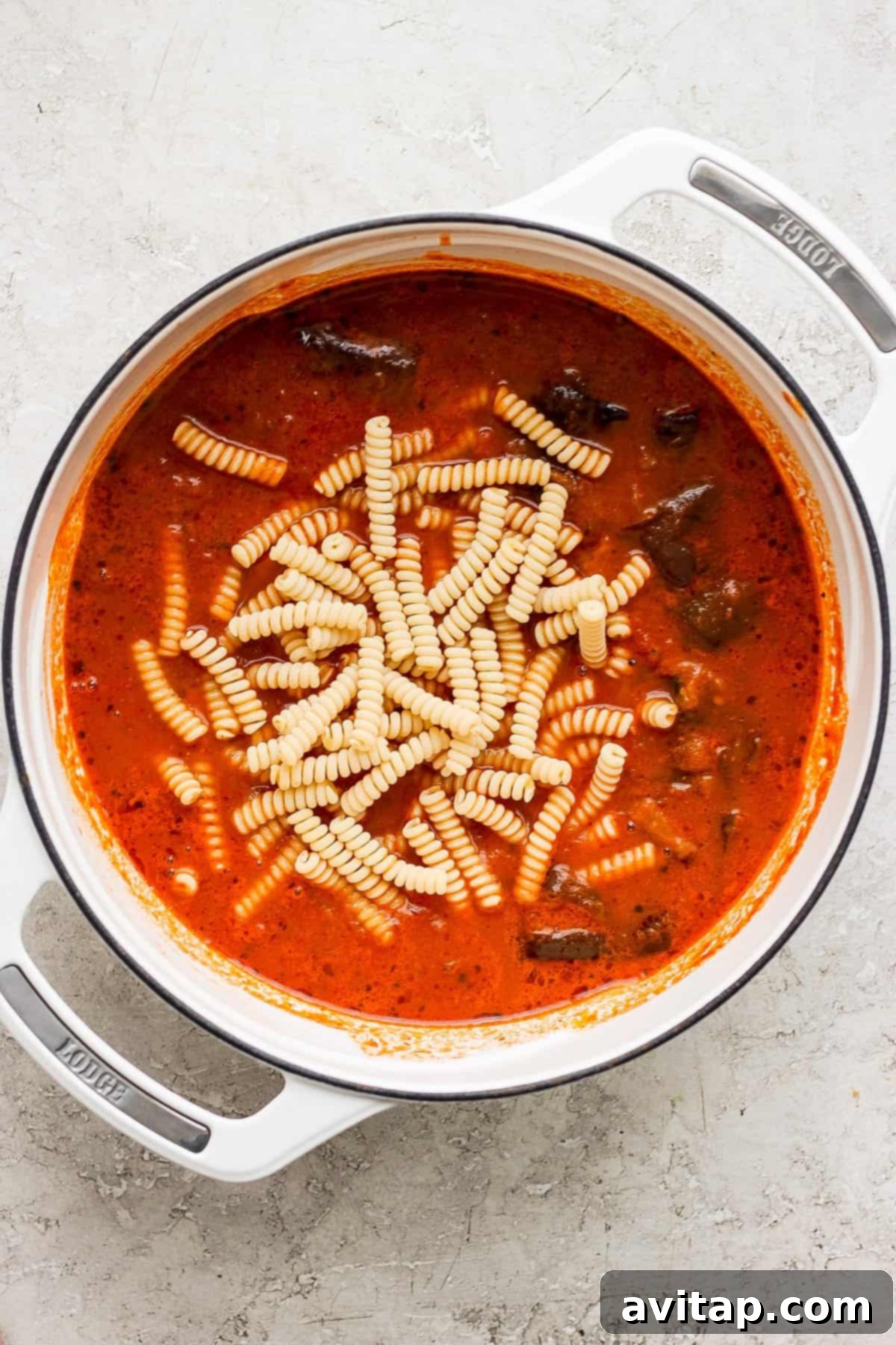 Easy One-Pot Pasta Alla Vodka 4 A simmering pot of rich tomato soup, featuring various pasta shapes, sits invitingly on a rustic kitchen counter.