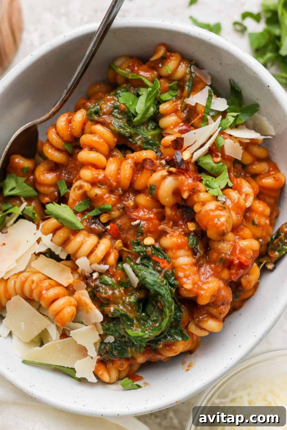 Easy One-Pot Pasta Alla Vodka 6 A close-up of fusilli pasta bathed in a rich tomato sauce, mixed with vibrant spinach, and crowned with delicate shavings of parmesan cheese, ready for a satisfying meal.