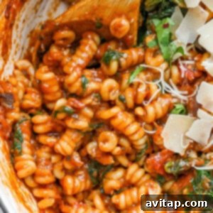 A close-up image of a pasta dish with tomato sauce, garnished with spinach and sprinkled with shredded cheese.