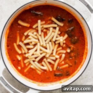 A pot of tomato soup with rigatoni pasta, simmering on a kitchen counter.