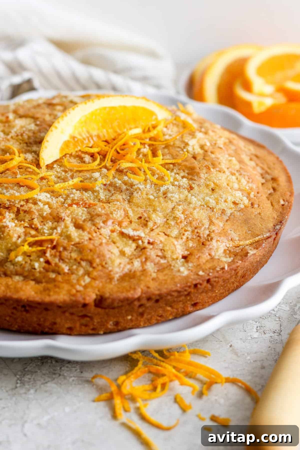 Orange Olive Oil Cake 2 A freshly baked orange olive oil cake garnished with bright orange zest on a pristine white plate, ready to be served.