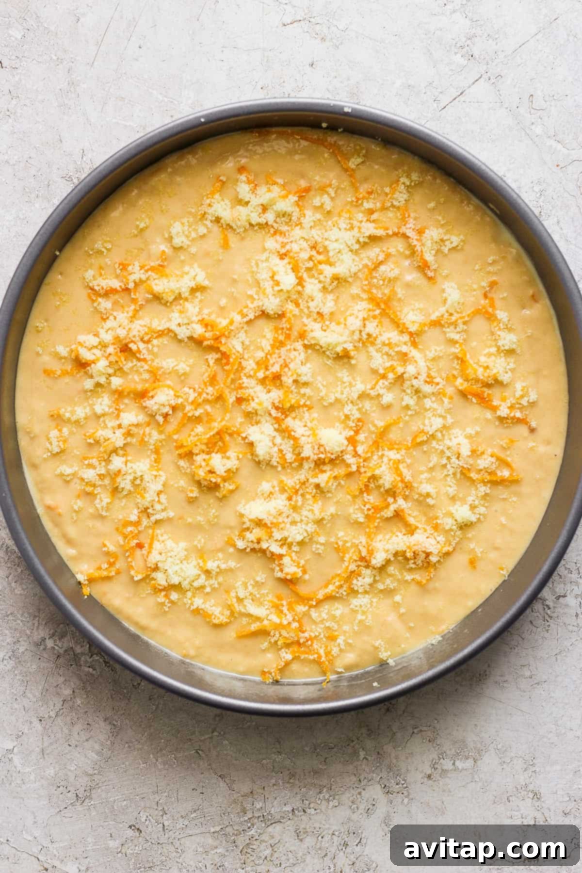 Orange Olive Oil Cake 3 An unbaked orange olive oil cake batter topped with orange zest sugar, ready for the oven in a round baking pan.