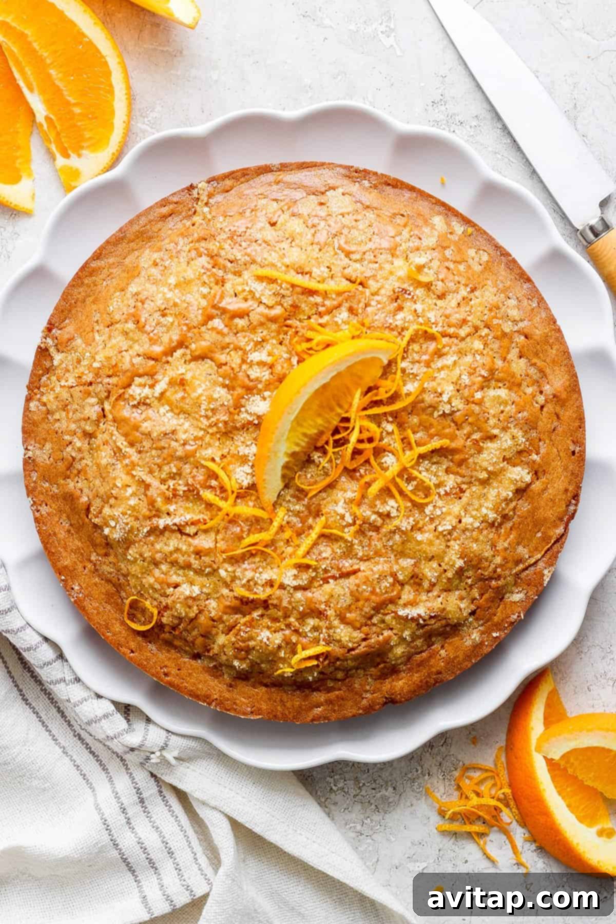 Orange Olive Oil Cake 4 A beautifully baked orange olive oil cake garnished with fresh orange zest on a white plate, accompanied by vibrant orange slices, creating a fresh and appealing presentation.