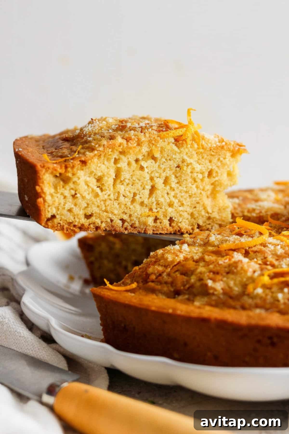 Orange Olive Oil Cake 6 A freshly baked orange olive oil cake with a slice partially lifted out, revealing its moist and tender crumb, beautifully topped with fine orange zest.