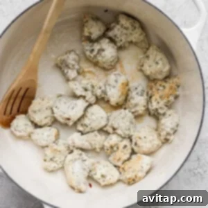 Chicken pieces being cooked in a white pot with a wooden spoon.