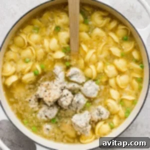 Pot of chicken noodle soup with green peas and a wooden spoon.