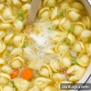 A pot of tortellini soup with carrots, peas, and grated cheese on top, with steam rising.