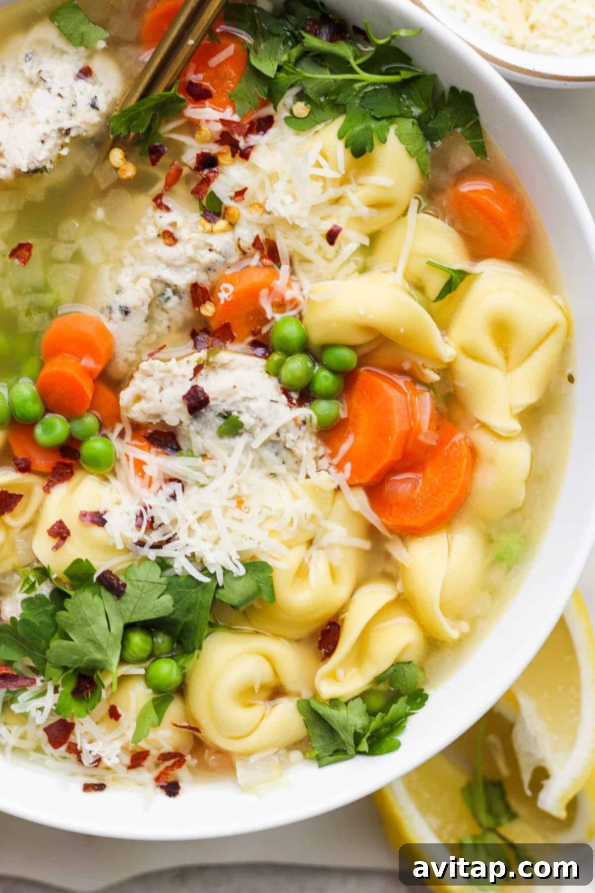 A comforting bowl of chicken noodle soup with vibrant vegetables, garnished with fresh parsley and grated cheese.