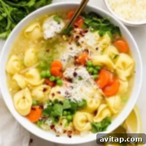 A bowl of tortellini soup with carrots, peas, and garnished with parsley and grated cheese, ready to be served.