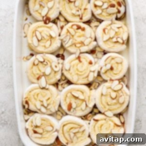 Unbaked cinnamon rolls arranged in a baking dish with slivered almonds on top.