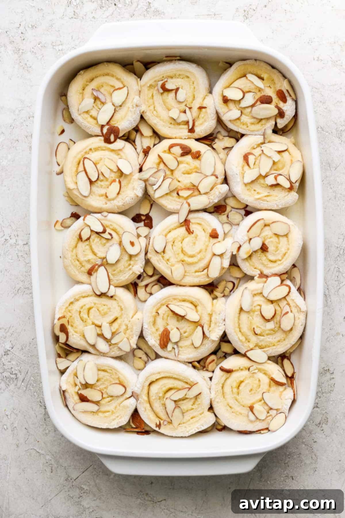 A close-up view of a baked Almond Croissant Cinnamon Roll, showcasing its fluffy texture, golden crust, and visible frangipane swirl.