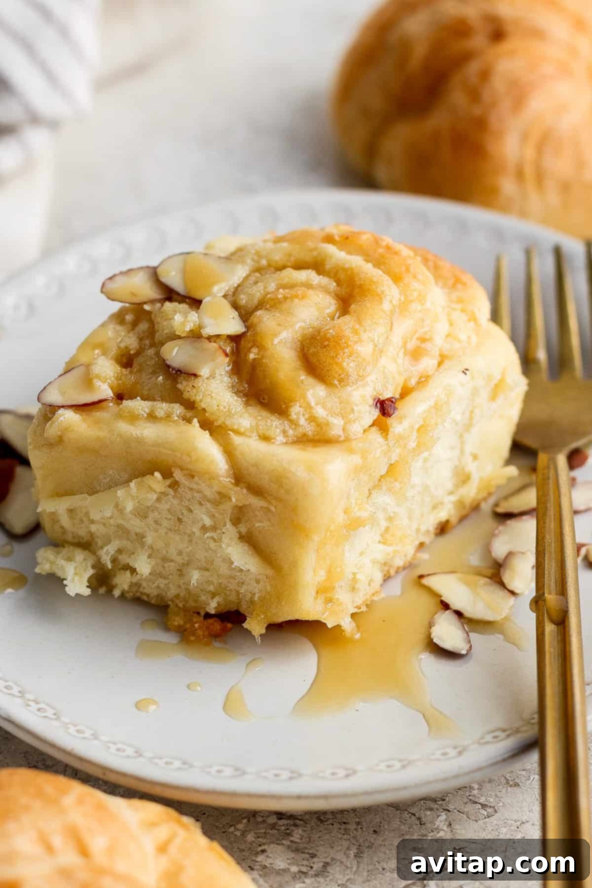 A stack of three golden-brown Almond Croissant Cinnamon Rolls, generously glazed and ready to serve on a rustic wooden board.