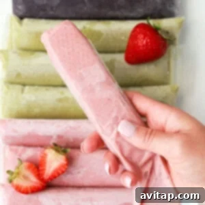 A person holding a strawberry popsicle in front of a pile of fresh strawberries, suggesting a refreshing treat.