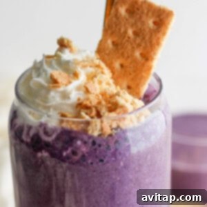 A creamy purple smoothie topped with whipped cream and crumbled biscuits, accompanied by a whole biscuit, presented invitingly.