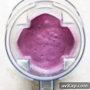 Top view of a blender jug filled with freshly blended purple smoothie, situated on a light-colored background, ready for serving.