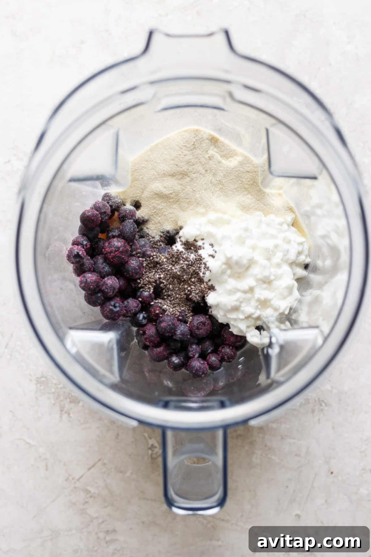 Top view of a high-speed blender containing fresh blueberries, creamy yogurt, chia seeds, and vanilla protein powder, ready to be blended into a smoothie.