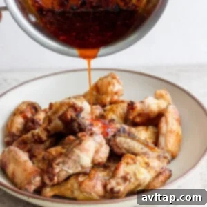 Pouring sauce over a plate of cooked chicken wings.