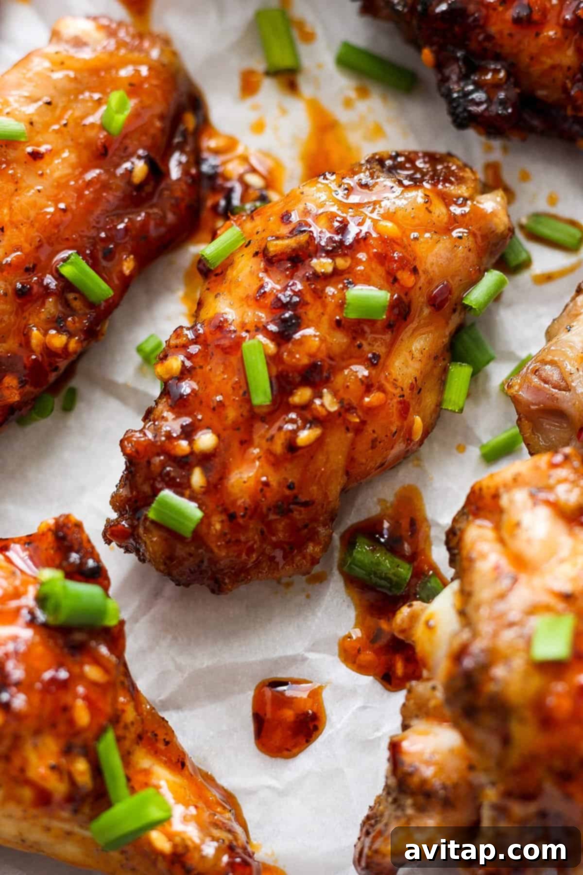 A vibrant close-up of beautifully glazed chicken wings, generously garnished with bright green chopped scallions and white sesame seeds, ready to be served.