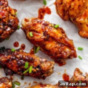 Glazed chicken wings on parchment paper garnished with sesame seeds and chopped green onions, ready to be served.