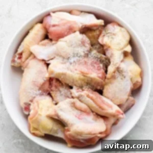 A bowl of raw chicken wings seasoned with spices.