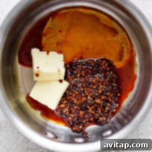 Ingredients in a saucepan including butter, chili flakes, and a dark liquid, possibly soy sauce or vinegar, preparing for a recipe.