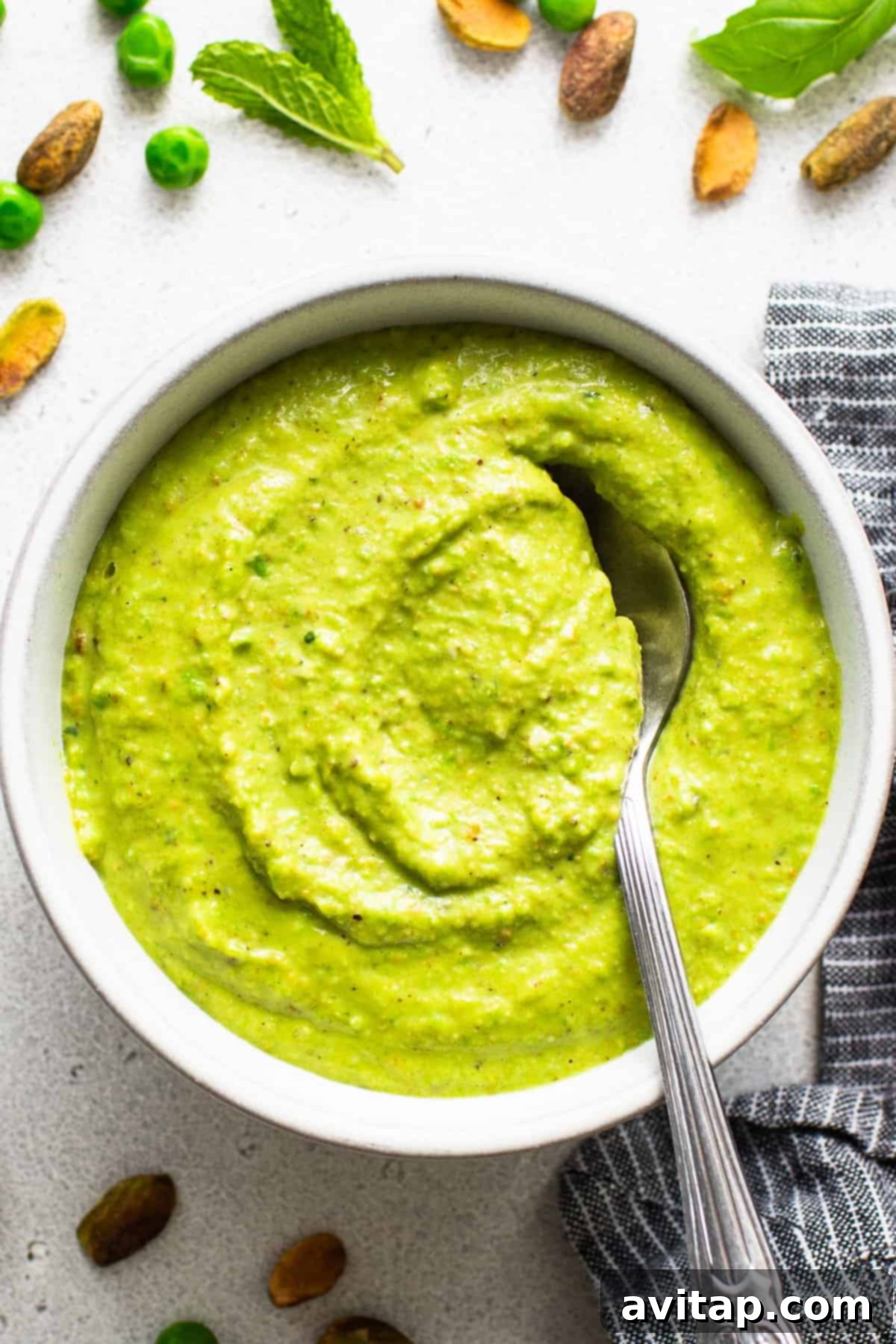 Fresh Sweet Pea Pesto Pasta 3 A close-up of creamy green pea and mint pesto, ready to be tossed with pasta, surrounded by fresh peas, mint leaves, and spices on a light surface.
