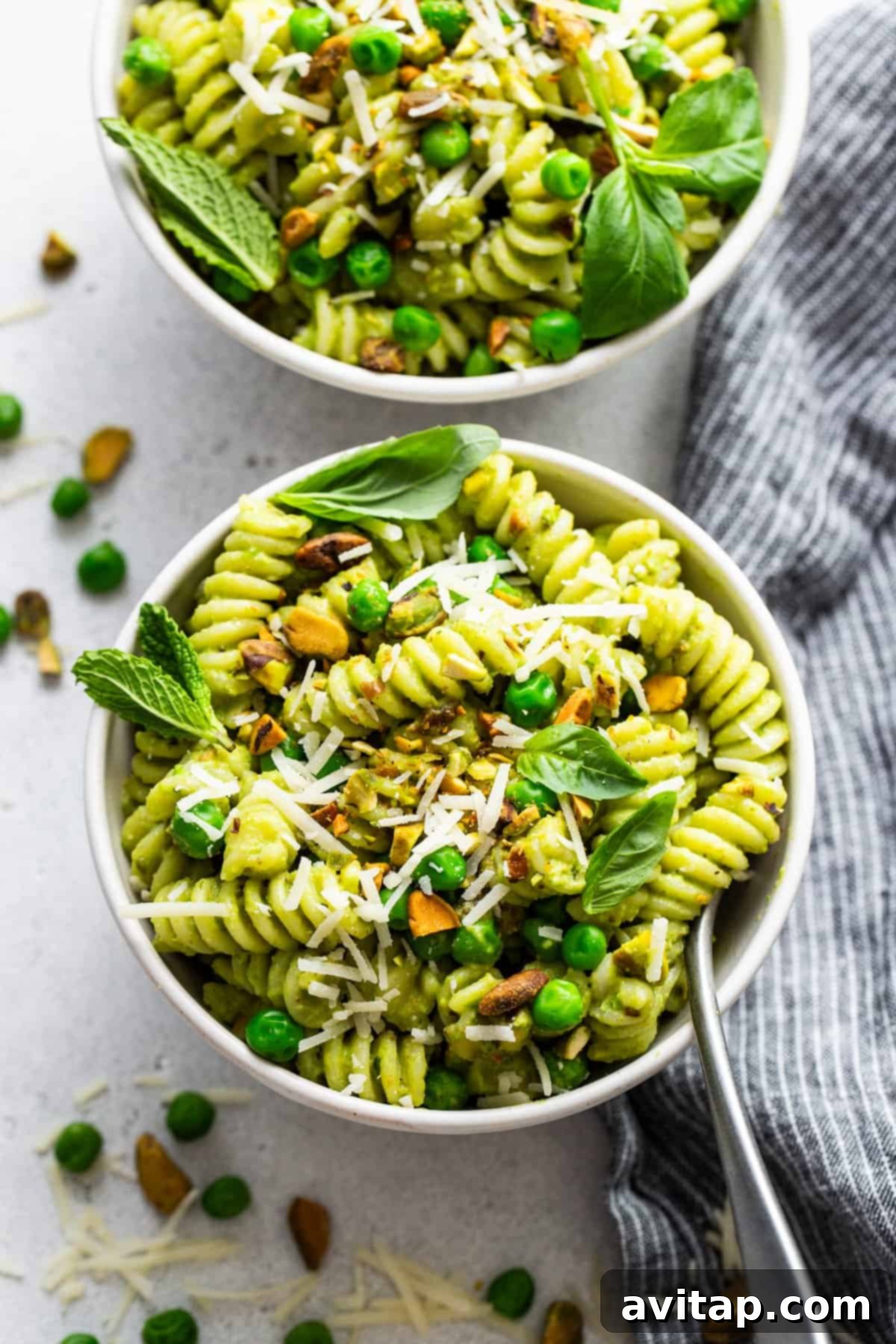 Fresh Sweet Pea Pesto Pasta 5 A close-up of a bowl of Sweet Pea Pesto Pasta garnished with peas, pistachios, basil leaves, and grated cheese, beautifully arranged on a light surface.