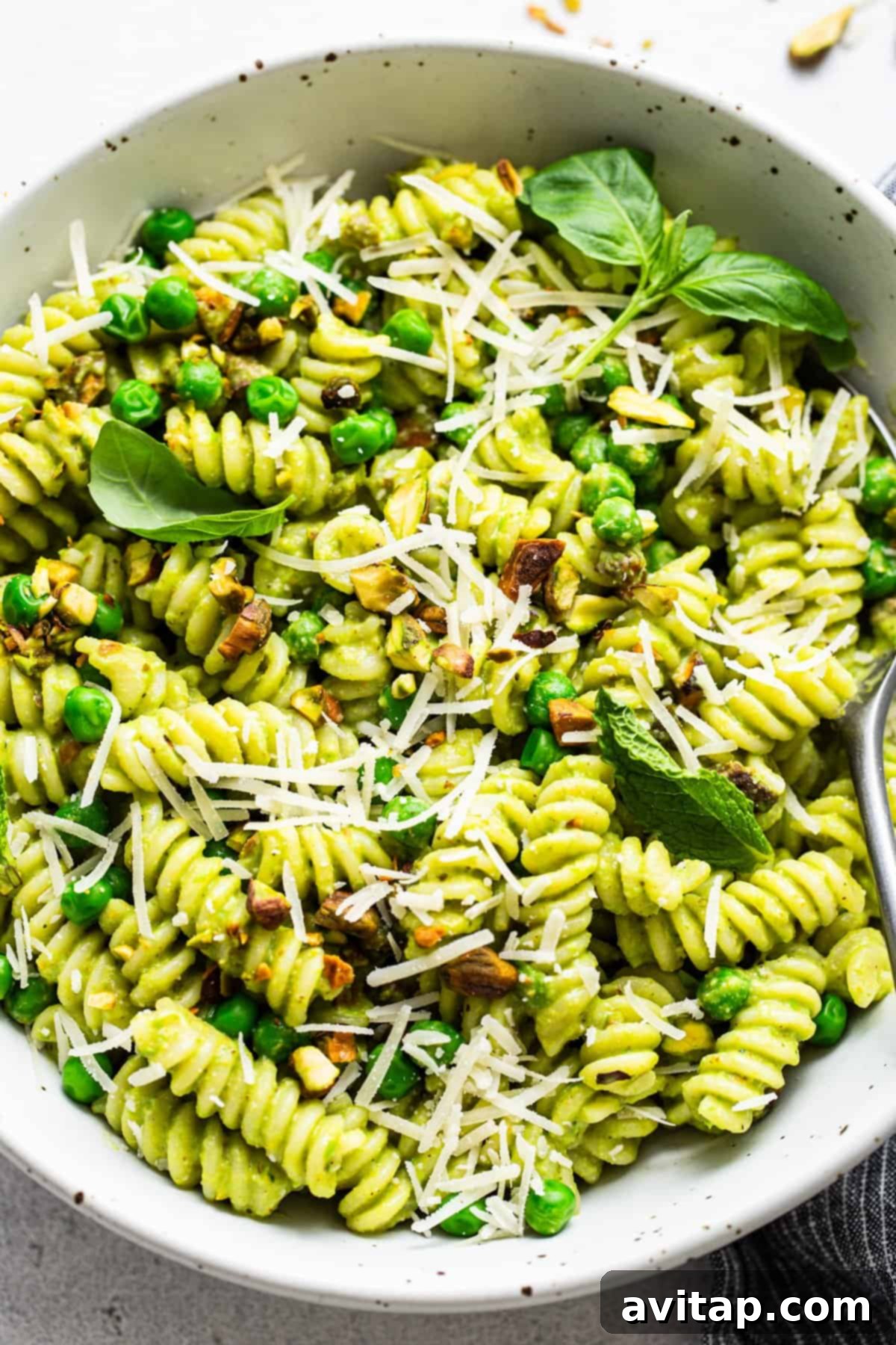Fresh Sweet Pea Pesto Pasta 6 A serving of Sweet Pea Pesto Pasta with peas and a generous sprinkle of grated cheese, garnished with fresh herbs, ready to be enjoyed.