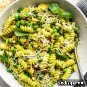 A bowl of Sweet Pea Pesto Pasta garnished with peas, grated cheese, and basil leaves, showcasing the vibrant colors.