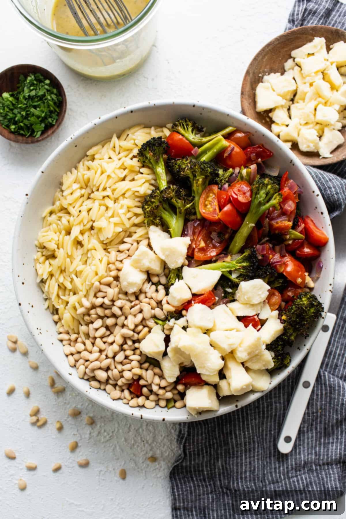 A close-up of a rustic white bowl overflowing with Orzo Pasta Salad, garnished with fresh parsley, showing the mix of pasta, roasted vegetables, and creamy cheese.