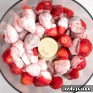 A food processor bowl filled with whole frozen strawberries and scoops of vanilla ice cream, viewed from above, ready to be blended into a creamy Dole Whip.