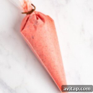 A piping bag filled with pink frosting, tied at the top, resting on a white marble surface, ready for chilling or immediate use.