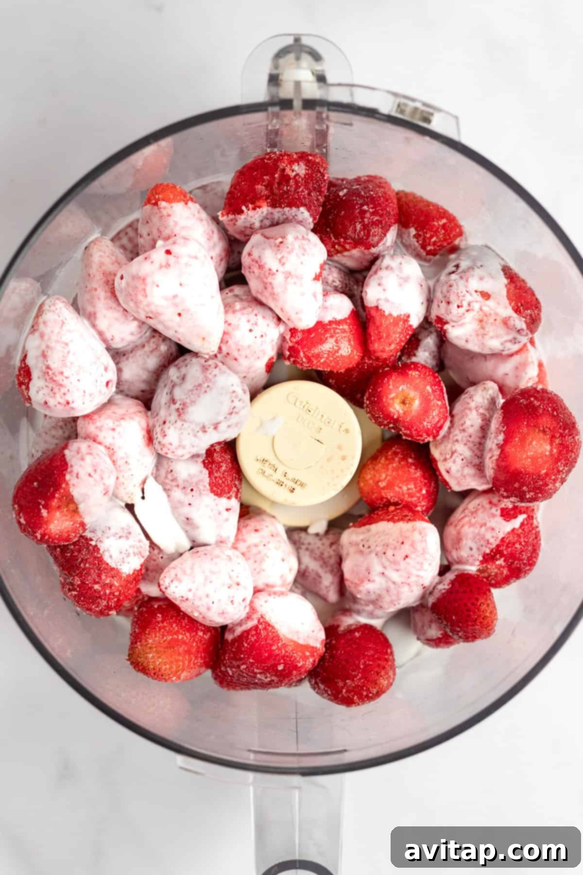 Strawberry Dole Whip 4 A food processor bowl filled with whole frozen strawberries and scoops of vanilla ice cream, viewed from above, ready for blending.