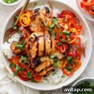 Grilled chicken thighs on a bed of white rice, garnished with sliced bell peppers, onions, and herbs in a bowl, with chopsticks on the side.