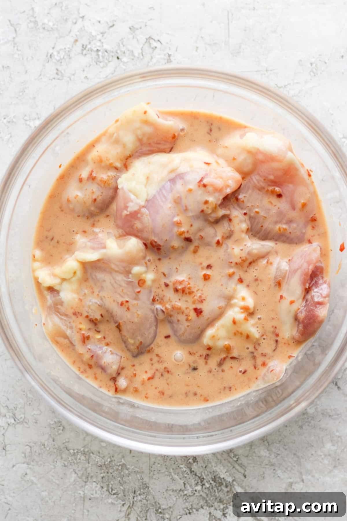 Tropical Grilled Coconut Chicken 3 Raw chicken thighs marinating in a bowl with sauce.