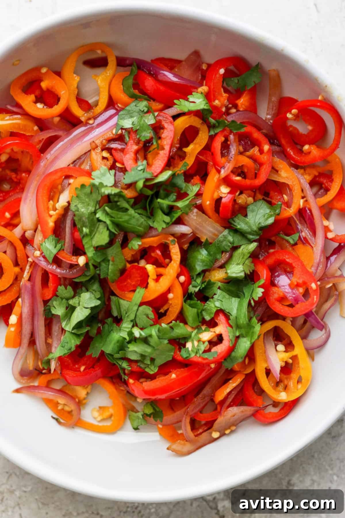 Tropical Grilled Coconut Chicken 5 A bowl of sliced red onions, red and orange bell peppers, garnished with fresh cilantro.