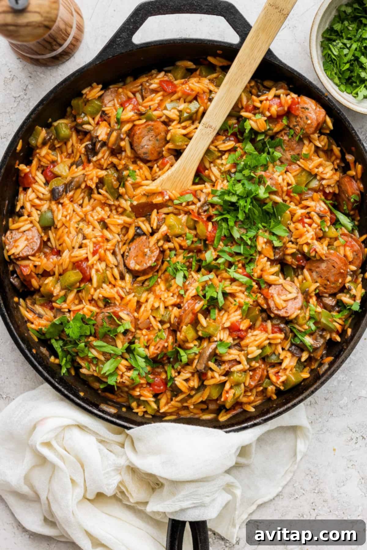 A skillet full of orzo pasta and vegetables with a wooden spoon, ready to serve.