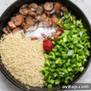 Orzo, spices, and tomato paste added to the skillet with vegetables and sausage.