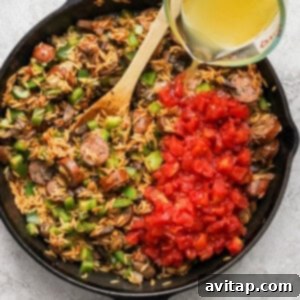 A person pouring chicken broth into a skillet with orzo and ingredients.