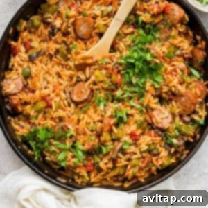 A skillet full of orzo pasta and vegetables with a wooden spoon, ready to serve.