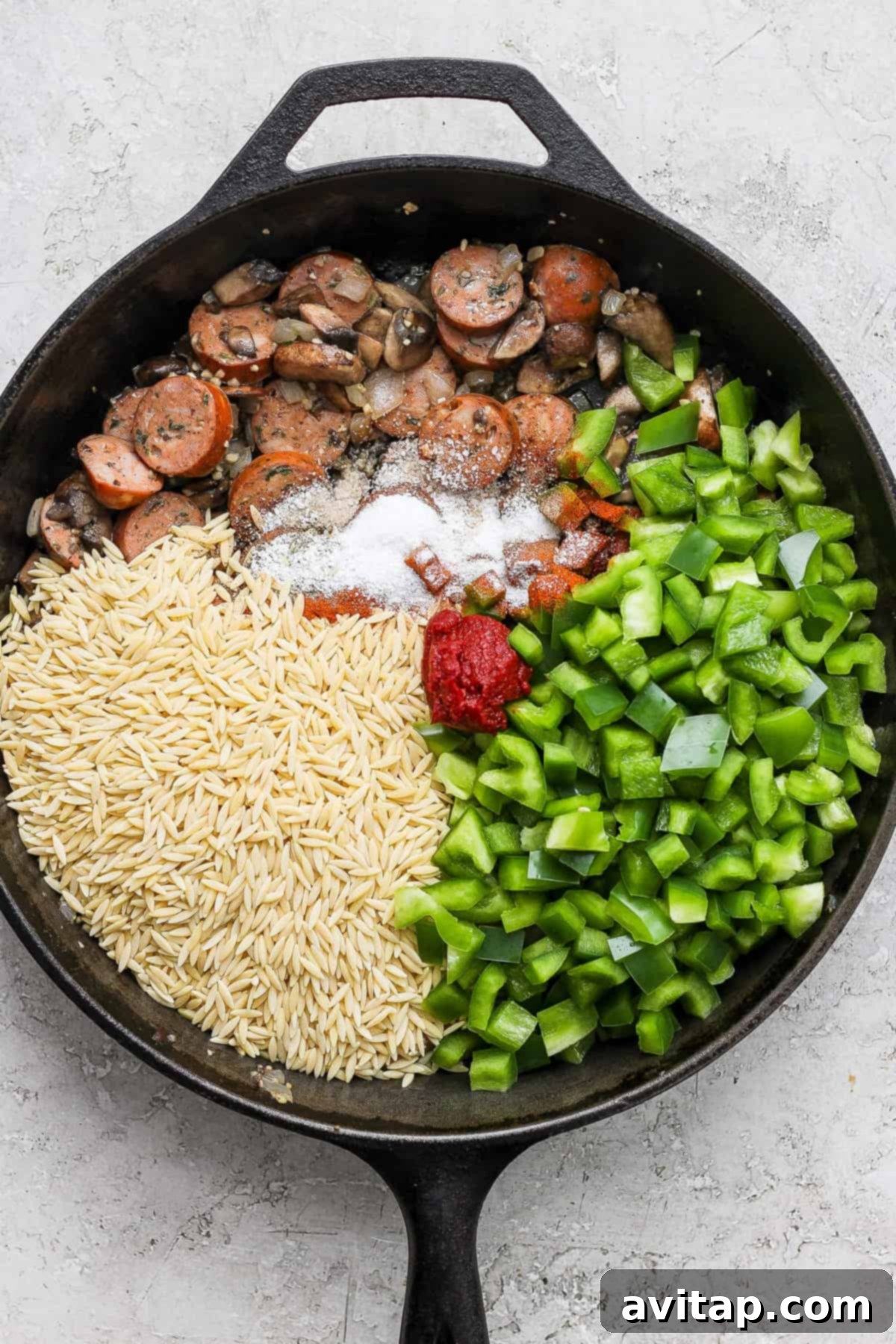 A frying pan with orzo, mushrooms and green peppers cooking.