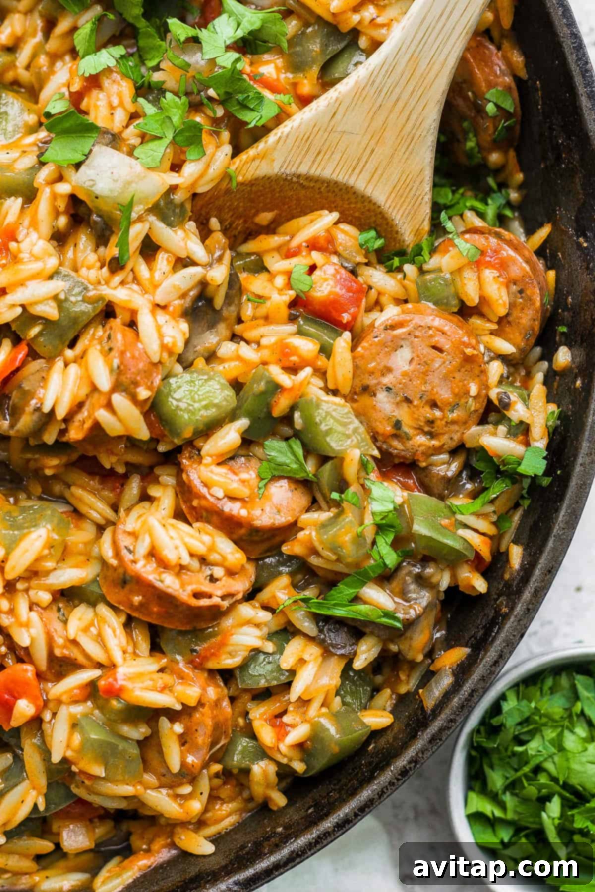 Sausage and orzo pasta in a skillet with a wooden spoon.