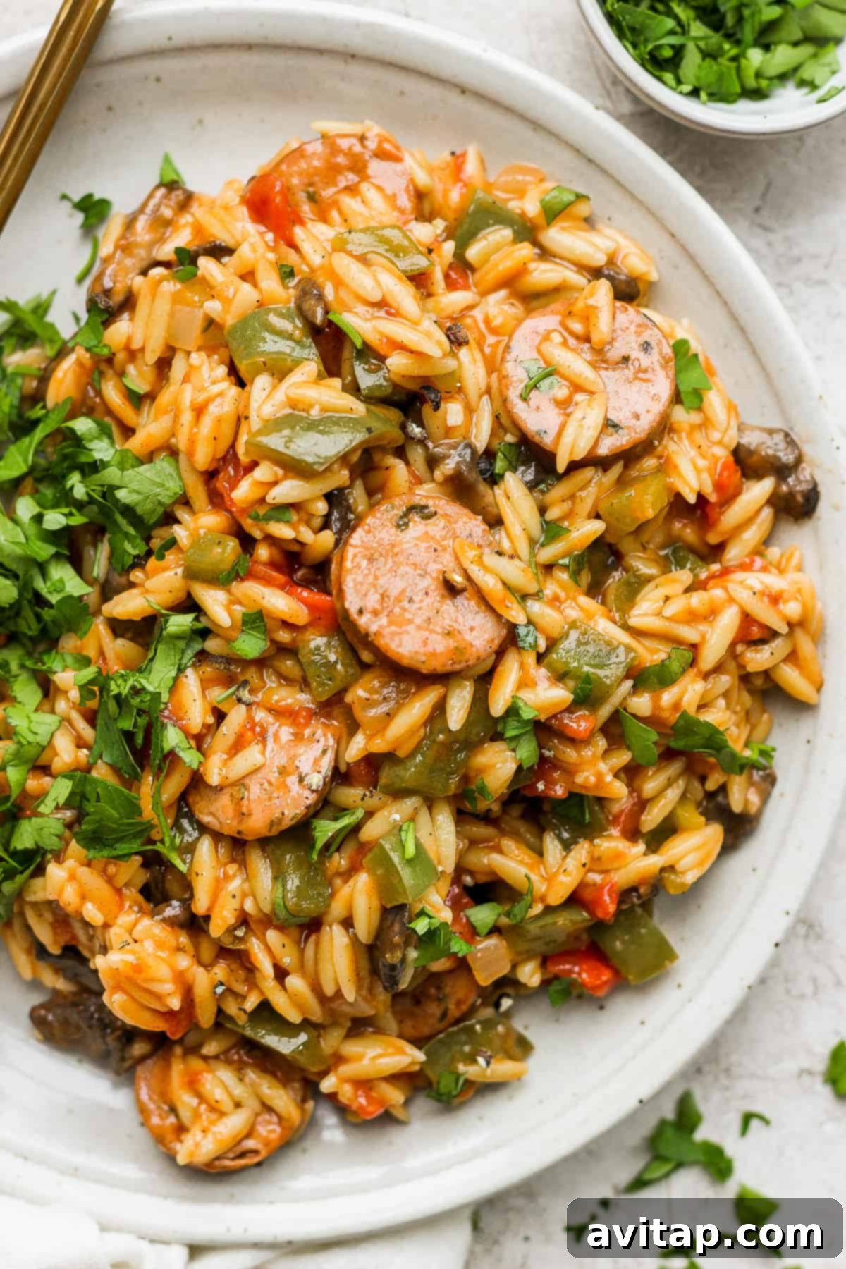 A plate of sauteed orzo with chicken sausage and vegetables, ready to eat.