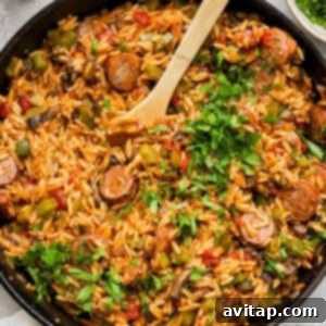Sausage and orzo pasta in a skillet with a wooden spoon.